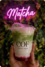 A COF matcha drink held up under a neon Matcha sign